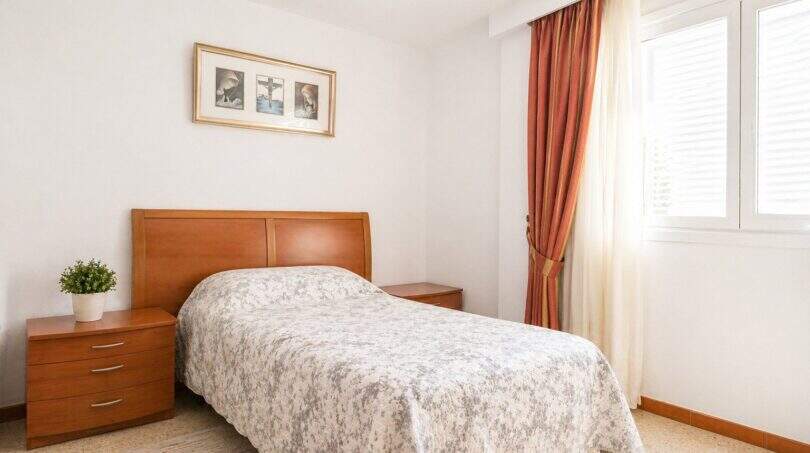 Schlafzimmer der Wohnung in Portixol mit Doppelbett, Holzmöbeln und roten Vorhängen am Fenster.