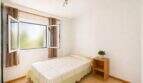 Helles Schlafzimmer der Wohnung in Portixol mit Einzelbett, Holzregal und geöffnetem Fenster mit Gardinén.
