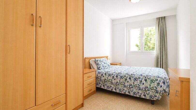 Helles Schlafzimmer der Wohnung in Portixol mit Holzschrank, Doppelbett und Fenster mit Grünblick.