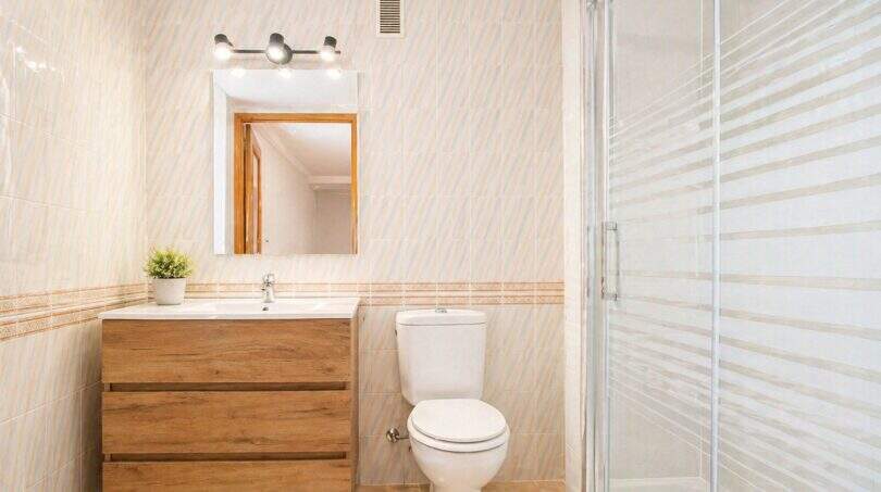 Helles Badezimmer der Wohnung in Portixol mit Holzunterschrank, Duschkabine und beigen Fliesen.