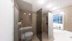 Modernes Penthouse-Bad mit Glasdusche, Holzoptik-Fliesen und Blick ins lichtdurchflutete Wohnzimmer