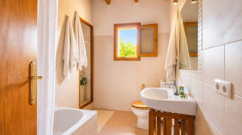 Baño luminoso de la finca con vigas de madera, bañera, lavabo y ventana con vista al jardín.