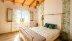 Dormitorio luminoso de la finca con techo de vigas de madera, cama doble y papel pintado botánico en Lloret de Vistalegre.