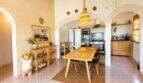 Comedor luminoso con mesa de madera, arcos y cocina abierta en finca mallorquina en Lloret de Vistalegre