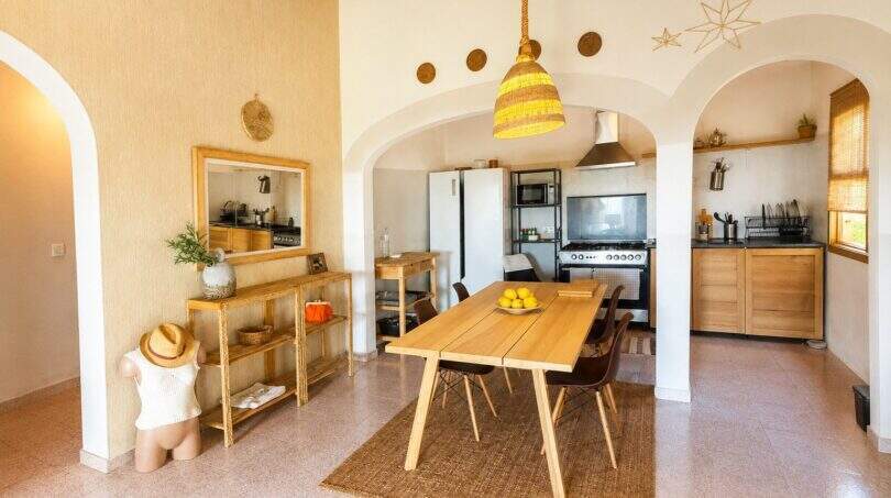 Comedor luminoso con mesa de madera, arcos y cocina abierta en finca mallorquina en Lloret de Vistalegre
