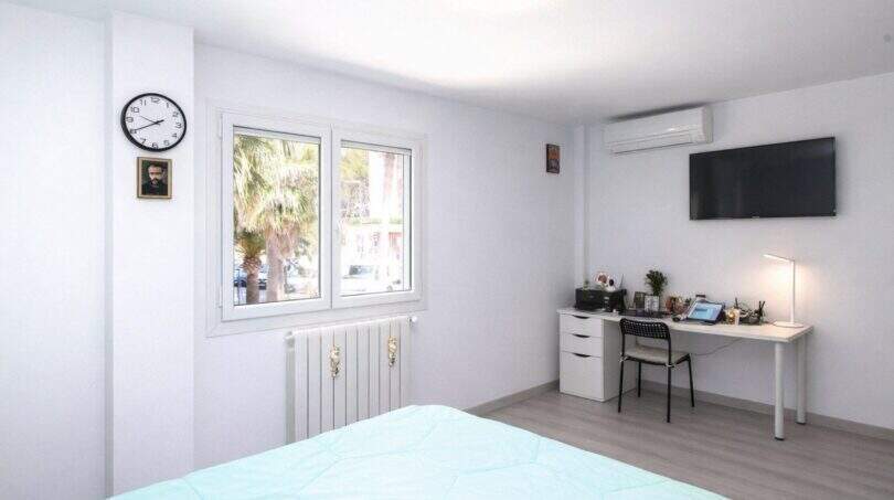 Helles Schlafzimmer mit Schreibtisch, TV, Klimaanlage und Fenster mit Palmenblick in Palma de Mallorca.