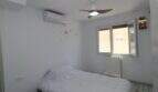 Helles Schlafzimmer mit Einzelbett, Klimaanlage, Deckenventilator und Heizkörper am Fenster.
