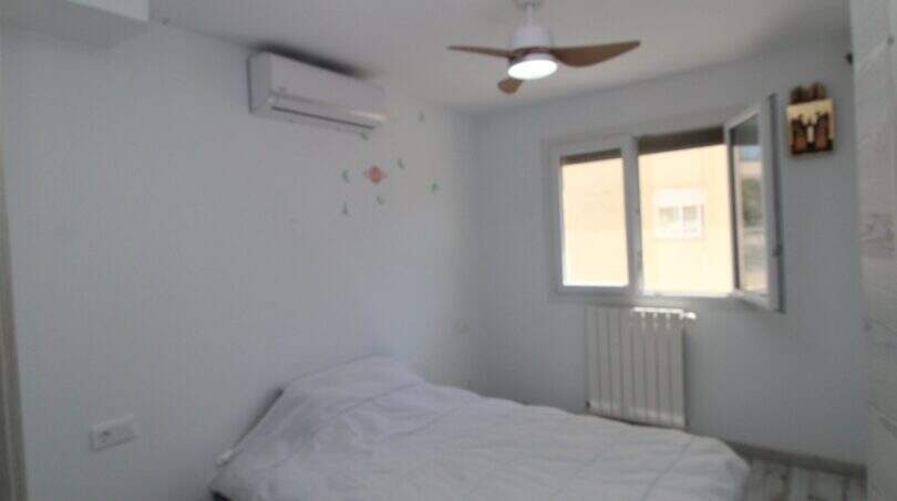 Helles Schlafzimmer mit Einzelbett, Klimaanlage, Deckenventilator und Heizkörper am Fenster.