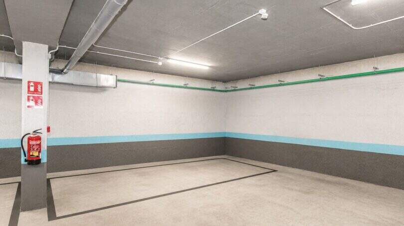 Privater Tiefgaragenstellplatz der Luxuswohnung in Palma mit Betonboden, Feuerlöscher und moderner Beleuchtung.