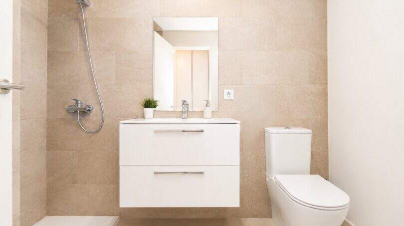 Modernes Badezimmer der Wohnung in Palma mit beigen Fliesen, schwebendem Waschtisch, Dusche und WC.