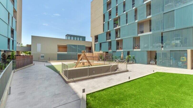Moderner Innenhof der Wohnanlage in Palma mit Kinderspielplatz, Rasenfläche und türkisfarbener Fassade