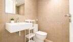 Helles Badezimmer der Palma-Wohnung mit Wandmontage-Waschbecken, WC und beigen Großformat-Fliesen.