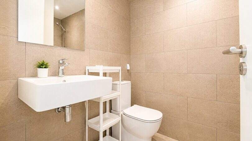 Helles Badezimmer der Palma-Wohnung mit Wandmontage-Waschbecken, WC und beigen Großformat-Fliesen.