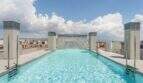 Infinity-Pool auf dem Dach mit Wasserfall und Stadtpanorama von Palma de Mallorca unter blauem Himmel.
