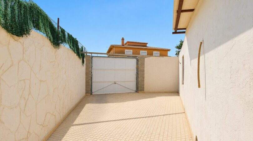 Geräumige Einfahrt mit weißem Tor, hellen Steinmauern und Blick auf das mediterrane Fincahaus in Palma