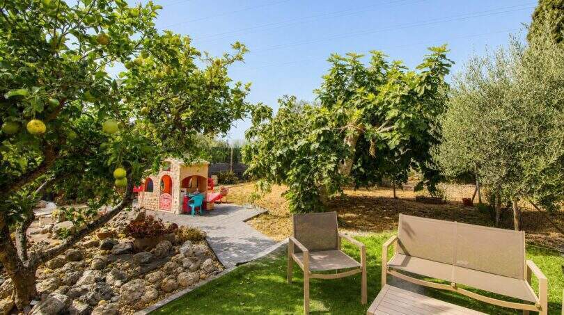 Sonniger Garten der Finca mit Sitzbereich, Obstbäumen und Kinderspielhaus nahe Palma de Mallorca.