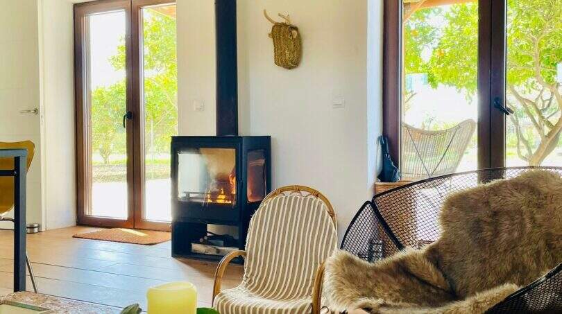 Helles Wohnzimmer der Finca Campanet mit Kaminofen, Naturholzboden und Blick in den grünen Garten.