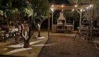 Abendliche Gartenanlage der Finca in Campanet mit beleuchtetem Pergola-Grillbereich und Sitzecke unter Bäumen.