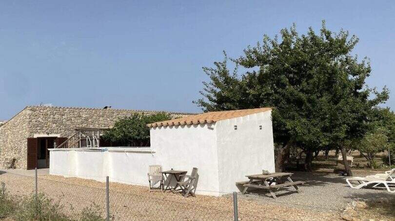 Finca Campanet: Weißes Nebengebäude mit Terrasse, Picknicktisch und Liegestühlen unter Bäumen, Steinhaus im Hintergrund.