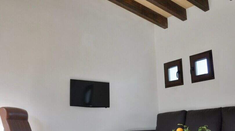 Wohnzimmer der Finca Campanet mit Holzbalkendecke, Deckenventilator, Ledersofa und Kuhfellteppich.