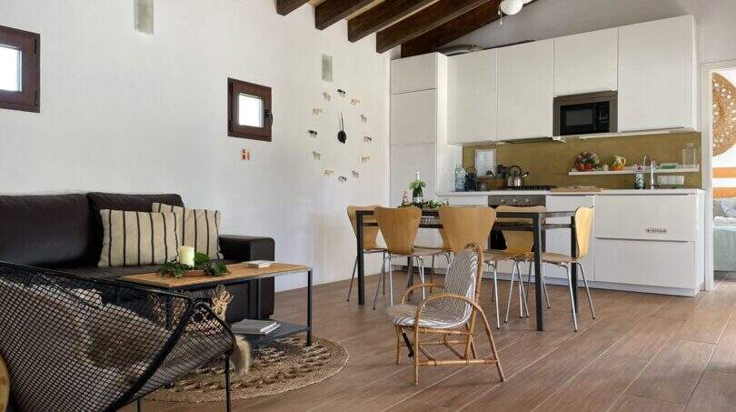 Offener Wohn-Kochbereich der Finca in Campanet mit Holzbalkendecke, Deckenventilator und moderner weißer Küche.