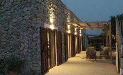 Finca Campanet: Terraza de piedra natural iluminada con contraventanas de madera y pérgola al atardecer