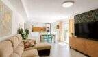 Helles Wohnzimmer mit Sofa, tropischer Tapete, TV und offener Küche in Finca bei Palma de Mallorca