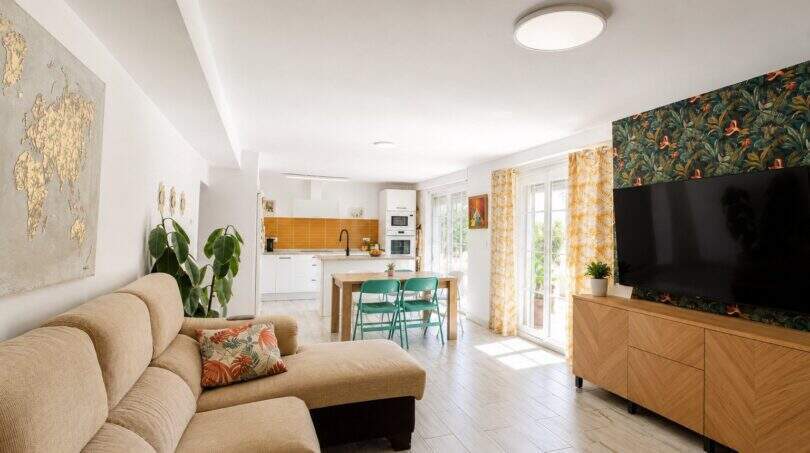 Helles Wohnzimmer mit Sofa, tropischer Tapete, TV und offener Küche in Finca bei Palma de Mallorca
