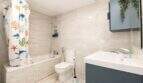 Helles Badezimmer mit Badewanne, buntem Duschvorhang, WC und blauem Waschtischunterschrank