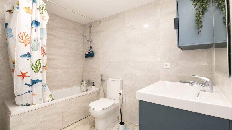 Helles Badezimmer mit Badewanne, buntem Duschvorhang, WC und blauem Waschtischunterschrank