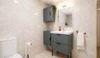 Modernes Badezimmer der Finca bei Palma mit grauem Waschtischunterschrank, Wandspiegel und hellen Marmorfliesen.