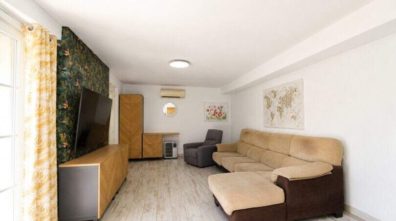 Helles Wohnzimmer der Finca mit Ecksofa, TV-Wand, Tropentapete und Klimaanlage nahe Palma.