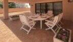Überdachte Terrasse der Wohnung in Palma mit weißen Gartenmöbeln, gedecktem Tisch und Blumenkübeln.