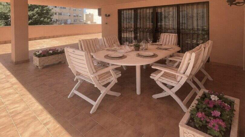 Überdachte Terrasse der Wohnung in Palma mit weißen Gartenmöbeln, gedecktem Tisch und Blumenkübeln.