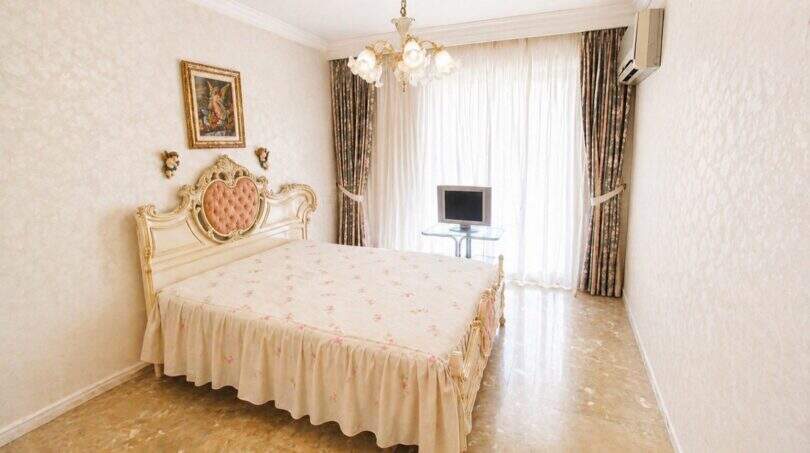 Elegantes Schlafzimmer mit Barockbett, Kronleuchter, Flachbildschirm und bodenlangen Vorhängen in Palma-Wohnung.