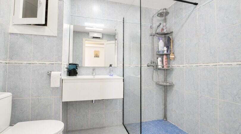 Modernes Badezimmer mit Glasdusche, blauem Mosaikboden und grauer Marmoroptik-Fliesen in Palma-Stadtwohnung