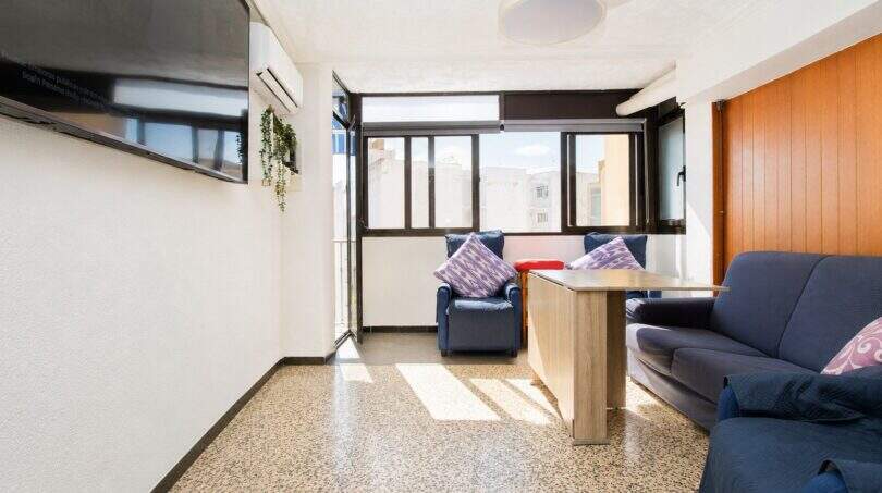 Helles Wohnzimmer mit blauen Sesseln, Sofa, Deckenventilator und großen Fenstern mit Stadtblick in Palma