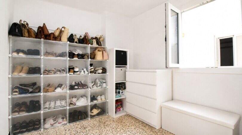Ordentlicher Abstellraum mit transparentem Schuhregalsystem, weißer Kommode und Sitzbank in Palma-Stadtwohnung.