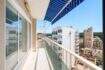 Sonniger Balkon mit blauem Sonnensegel und Stadtblick auf Palma de Mallorca, helle Glasfront