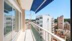 Sonniger Balkon mit blauem Sonnensegel und Stadtblick auf Palma de Mallorca, helle Glasfront