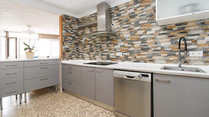 Moderne Küche mit Steinwand-Backsplash, grauen Schränken, Induktionskochfeld und Edelstahl-Dunstabzug in Palma-Stadtwohnung