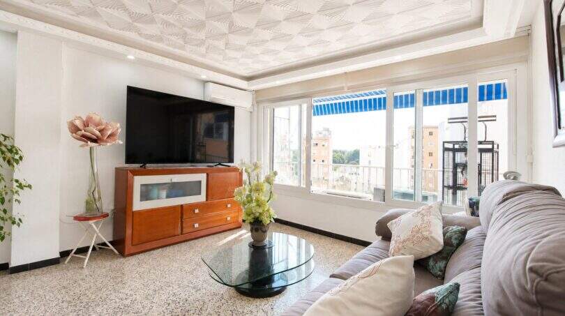 Helles Wohnzimmer mit Sofa, Flachbild-TV, Glastisch und großen Fenstern mit Stadtblick in Palma