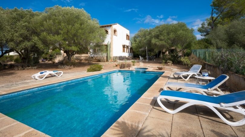 Villa Marratxí: Rechteckiger Pool mit Liegestühlen, weißes Ferienhaus, mediterrane Bäume, blauer Himmel.