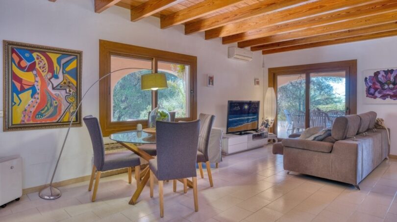 Lichtdurchflutetes Wohn-Esszimmer der Villa in Marratxí mit Holzbalkendecke, Glastisch und modernem TV-Bereich.