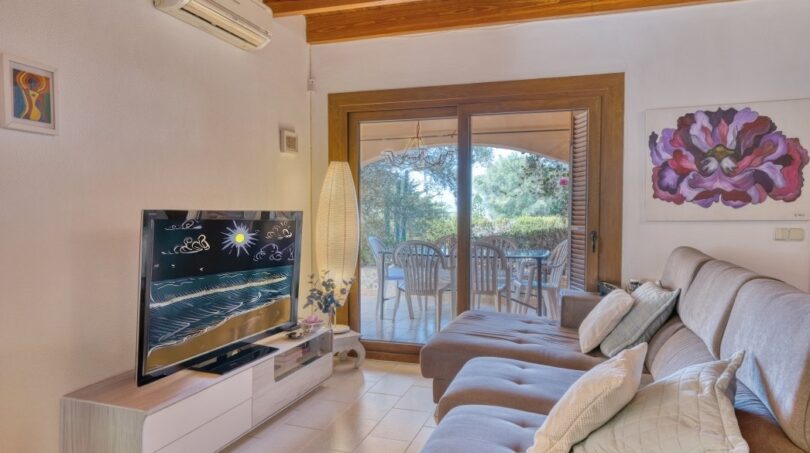 Helles Wohnzimmer der Villa in Marratxí mit Sofa, TV, Holzbalkendecke und Zugang zur Terrasse mit Gartenblick.