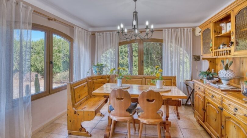 Helles Esszimmer der Villa in Marratxí mit rustikalen Holzmöbeln, Kronleuchter und Blick in den Garten.