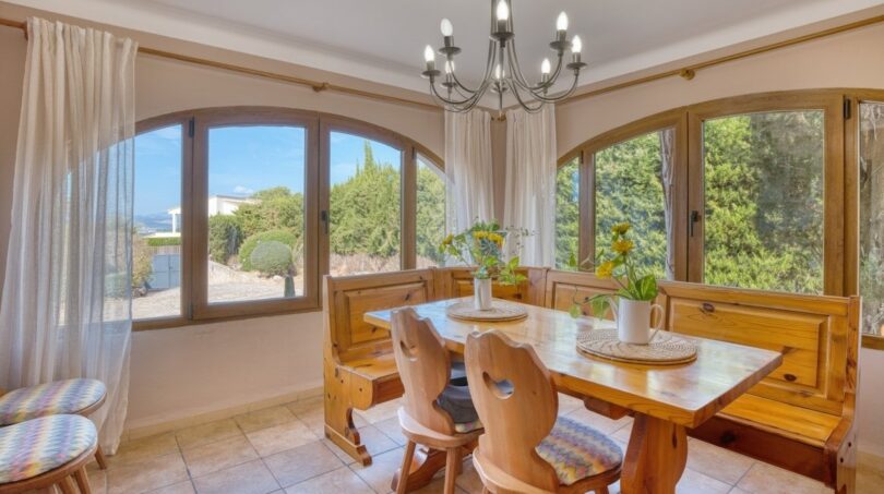 Helles Esszimmer der Villa in Marratxí mit Holzmöbeln, Kronleuchter und großen Bogenfenstern mit Gartenblick.
