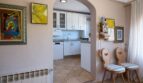 Wohnbereich mit Rundbogen zur weißen Küche, Terrakottaboden, Kunstwerken und Holzstühlen in Villa Marratxí