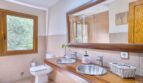 Badezimmer der Villa in Marratxí mit Doppelwaschbecken, Holzablage, großem Spiegel und Natursteinoptik-Fliesen.