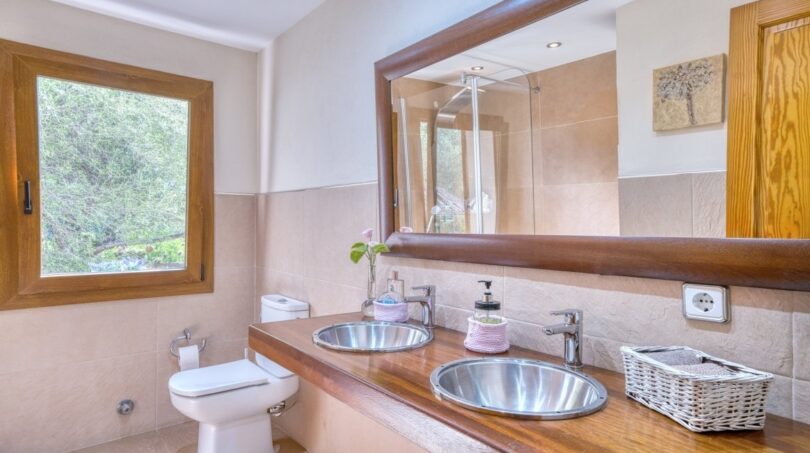 Badezimmer der Villa in Marratxí mit Doppelwaschbecken, Holzablage, großem Spiegel und Natursteinoptik-Fliesen.
